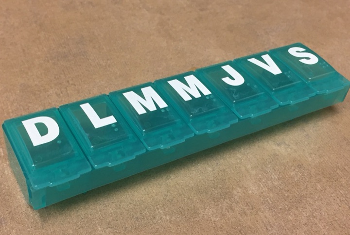 Teal weekly pill organiser with Spanish day letters on a wooden table