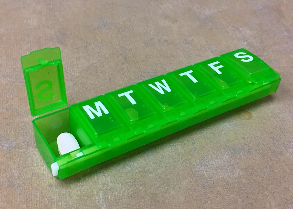 A green weekly pill organiser with one compartment open